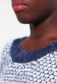 Stickad tröja med en marinblå, ludden halsringning, strukturerad vit och marinblå kropp, som har ett löst vävt mönster och en mysig känsla.