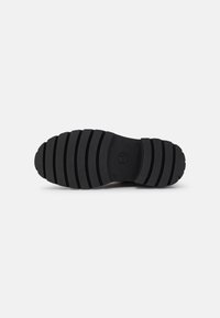 Semelle de chaussure noire avec des rainures horizontales, dotée d'un bout arrondi et d'une surface lisse. Logo du fabricant clairement imprimé sur la zone du talon.