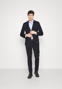 Completo navy sagomato con giacca strutturata e pantaloni slim-fit, abbinato a una camicia azzurro chiaro e mocassini neri.