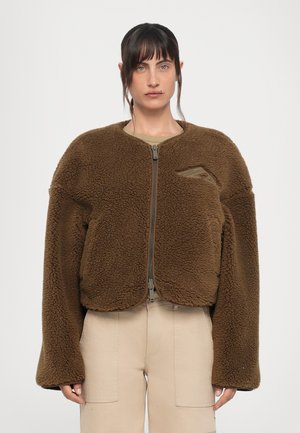 Brown fleece jacket with a round neckline, zip closure, and dropped shoulders. Features a small left chest pocket and soft texture.