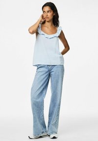 Ljusblå ärmlös topp med rynkad halsringning, i kombination med vida blekna jeans och vita sneakers. Slät tygkvalitet.