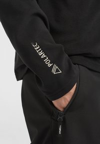 Sort fleece sweatshirt med et Polartec-logo på ærmet; blød tekstur med en lynlåslomme på siden, prydet med O'Neill-branding.
