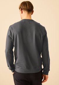Felpa grigia scura con maniche lunghe, collo a giro e una texture liscia, che mostra la vista posteriore su uno sfondo neutro.