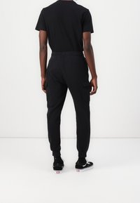 Černé bavlněné tričko kombinované s černými cargo joggery. Joggery mají boční kapsy a manžety na kotnících, v kombinaci s černými teniskami.