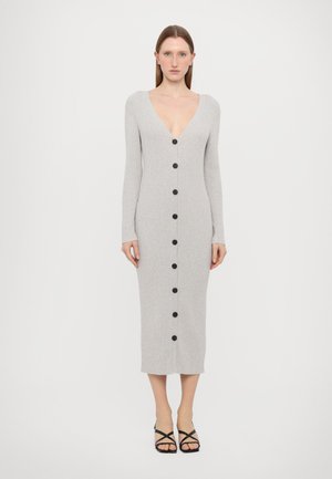 Robe grise à manches longues côtelées avec un décolleté en V profond, ornée de boutons noirs sur le devant et arrivant mi-mollet. Accessoirisée avec des sandales noires simples.