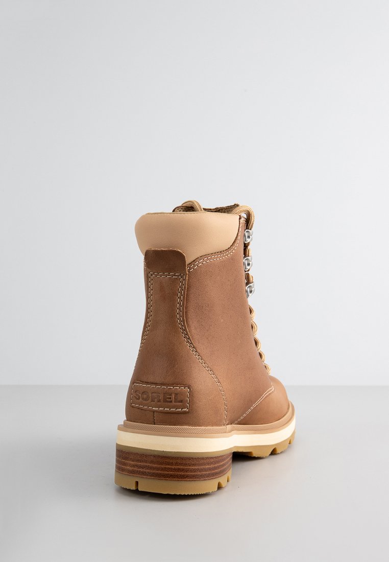 Braune Lederstiefel mit einem beigen Absatz, Schnürdesign, silbernen Ösen und einer strukturierten weißen Gummisohle. Verfügt über ein Logo-Patch an der Seite.