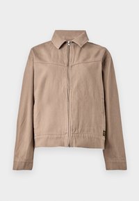 Tan cotton jacket with a collar, front zipper, and long sleeves. Features a textured fabric and a small logo tag at the hem.