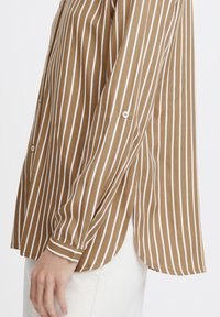 Brown and white striped button-up shirt, long sleeves, soft fabric, curved hem, slight side slits, and white button accents on sleeves.