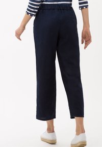 Pantalon court en lin bleu marine à coupe décontractée, taille élastique et détail bouton sur la poche arrière, associé à des espadrilles blanches.