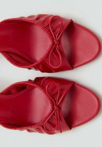 Chaussures en cuir rouge à enfiler avec une texture lisse, présentant un design plissé et un accent de nœud sur la partie supérieure, style à bout ouvert.