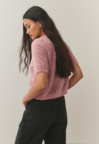 Rausvos spalvos pūkuotas trumpomis rankovėmis megztinis su tekstūruotu paviršiumi, derinamas su juodomis aukštakulnėmis džinsais. Megztinis šiek tiek trumpesnio kirpimo.