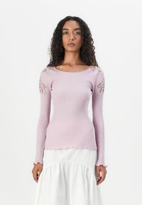Langwerpige, geribde roze top met een gegolfde zoom en kantaccenten op de schouders, gecombineerd met een witte, gelaagde rok.