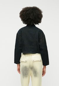 Skraćena crna traper jakna s visokim ovratnikom i spuštenim ramenima, uparena s svijetlim hlačama koje imaju stražnje džepove i izblijedjeli uzorak.