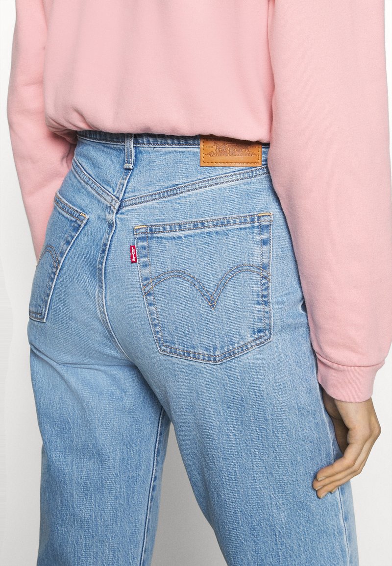 Helle blaue Denim-Jeans mit einer hohen Taille, ausgestattet mit kontrastierendem orangem Stich, einem Lederpatch und einem charakteristischen Design der Gesäßtasche.