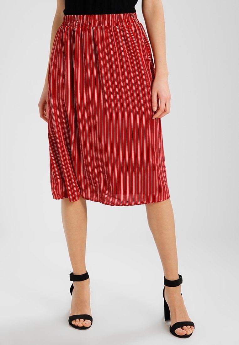 Femme portant une jupe mi-longue rayée verticalement rouge et blanche, un haut noir et des sandales noires à talons avec bride à la cheville.