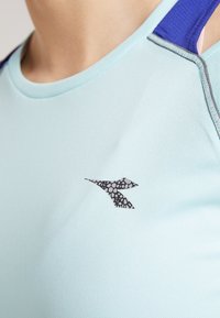 Light blue athletic top with a textured fabric, featuring a dark logo on the chest and a purple accent on the shoulder straps.