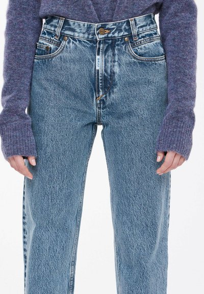 Lyseblå denimjeans med høyt liv, rette ben, og synlig søm. Kombinert med en lilla strikket genser.