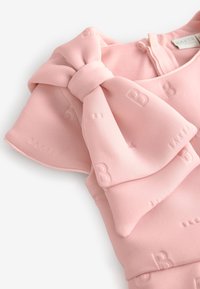 Rosa Kleid mit einem strukturierten Stoff und geprägten Buchstaben. Es hat ein großes Schleifendetail an der Schulter und einen Reißverschluss auf der Rückseite.