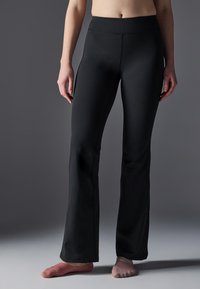 Pantaloni negri, care se potrivesc pe corp, din material elastic cu o textură netedă, cu fund îndoit și talie elastică înaltă, prezentați cu șosete asortate.