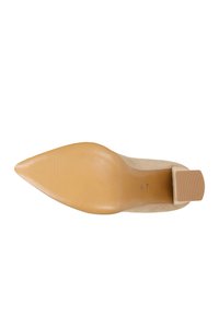 Beige semišová lodička na vysokém podpatku s špičatou špičkou, plochou hnědou gumovou podrážkou a malým blokovým podpatkem s vodorovnými drážkami na zadní straně.