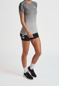 Szary sportowy T-shirt z krótkim rękawem i gradientowym wzorem; do tego czarne spodenki z białym wzorem w jodełkę po boku. Czarne tenisówki.