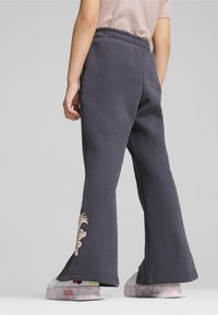 Grå sweatpants med flare-bund og elastisk talje, prydet med en lys rosa broderet design på underbenet. Sammen med hvide sko med et blomsterdesign.