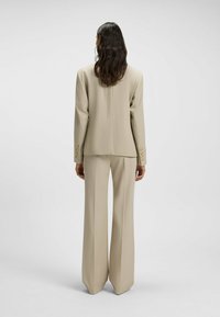 Beige tailored suit featuring a long, loose-fitting blazer and wide-leg trousers. Smooth fabric with minimal detailing and a classic cut.