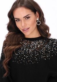 Fekete felső textúrált mintával, a nyakrészen szórt ezüst, arany és bronz flitterekkel. Nagy kör fülbevalók is tartoznak hozzá.