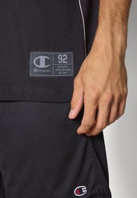 Černé sportovní šortky s síťovanou texturou. Obsahují nášivku s logem "Champion 92" a další malé logo na lemu.