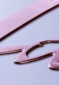 Rosa-goldene Flüssigkeit tropft auf eine glatte Oberfläche und zeigt eine glänzende Textur sowie ein flüssiges Design mit einer ausgeprägten Form und Wölbung.
