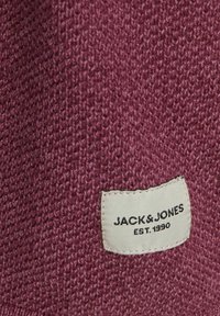 Burgundi spalvos megzta medžiaga su tekstūru; turi siuvinėtą smėlio spalvos etiketę su užrašu "JACK & JONES EST. 1990."