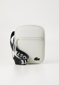 Borsa a tracolla bianca con superficie testurizzata, tasca con zip e tracolla nera con lettering bianco audace. Accento con logo coccodrillo verde.