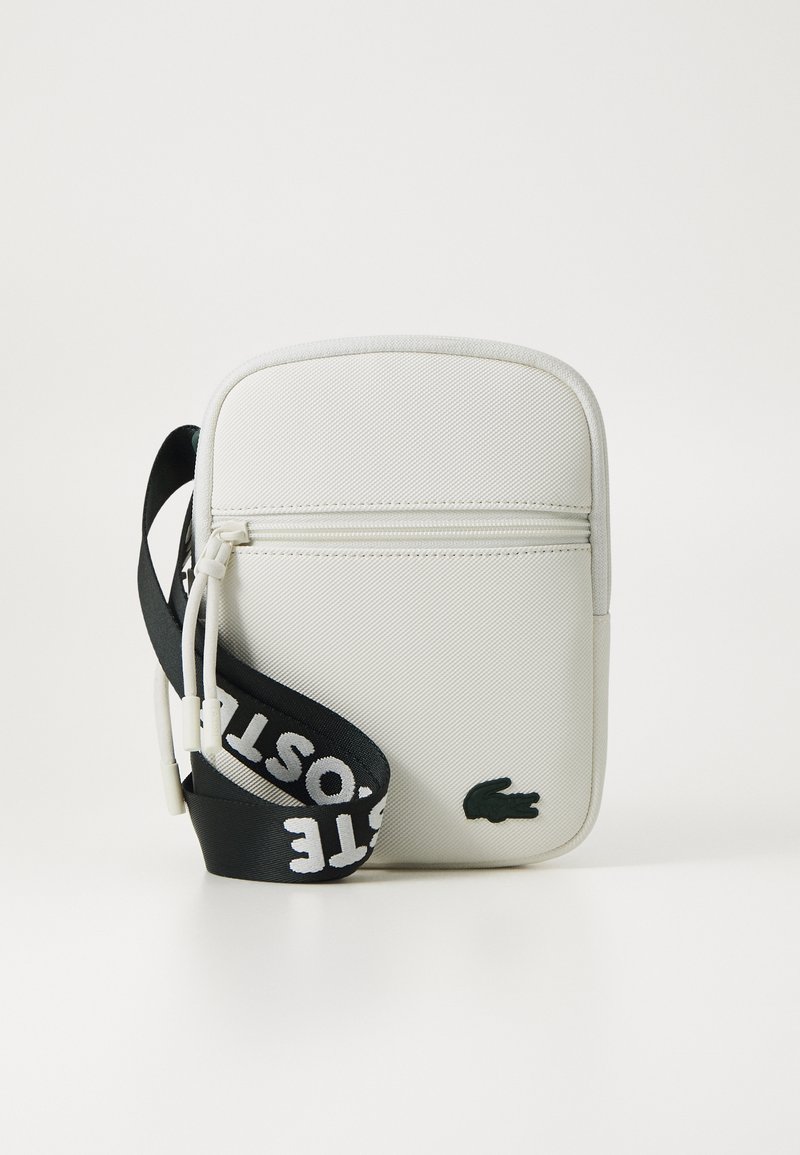 Borsa a tracolla bianca con superficie testurizzata, tasca con zip e tracolla nera con lettering bianco audace. Accento con logo coccodrillo verde.