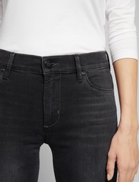 Schwarze Jeans aus Denim mit einem engen Design, ausgestattet mit einem Knopfverschluss vorne, Gürtelschlaufen und minimalen Nähten. Die Textur ist glatt.