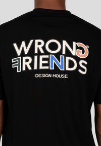 Černé tričko s krátkým rukávem, na zadní straně s velkým, vícebarevným textovým grafickým prvkem s nápisem "WRONG FRIENDS DESIGN HOUSE."