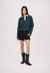 Tyrkysová košeľa s dlhým rukávom a bielym golierom, skombinovaná s čiernymi šortkami a čiernymi čižmami po kolená. Hladká textura, ležérny dizajn.