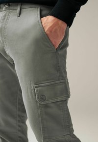 Cargo-Hosen aus leichtem grauem Baumwollmix, ausgestattet mit seitlichen Taschen mit Knopfverschlüssen. Glatte Textur und gerade Passform.