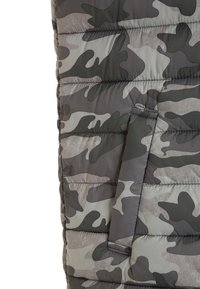 Maskovac�í péřová bunda v odstínech šedé a zelené, se štepovanou texturou a postranní kapsou. Materiál vypadá synteticky.