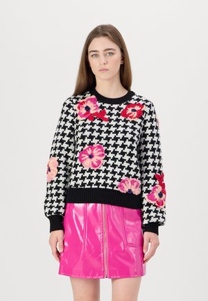 Gestickter schwarz-weißer Hahnentrittmuster-Pullover mit rosa floralem Stickereimuster, kombiniert mit einem glänzenden pinken Vinyl-Minikleid mit vorderen Reißverschlüssen.