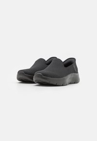 Black slip-on shoes made of breathable mesh with a textured surface. The flexible outsole has a subtle pattern for grip.