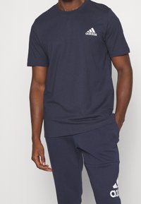 Námořnické modré sportovní tričko vyrobené z bavlněné směsi. Má kulatý výstřih a malé bílé logo Adidas na levém prsu. Měkká textilie.