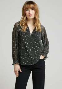 Blouse noire légère avec un col en V et des manches longues en voile. Présente un tissu texturé avec des accents floraux argentés. Ourlet arrondi.
