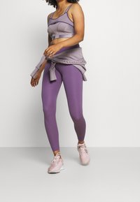 Fialový sportovní set obsahující texturovaný crop top se straps a legíny s vysokým pasem. Doplněno o měkk�é růžové sportovní boty.