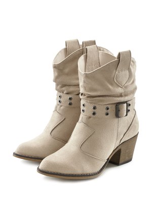 Stivaletti alla caviglia in suede beige con un design morbido, caratterizzati da una cintura decorativa con borchie metalliche e un tacco in legno impilato.