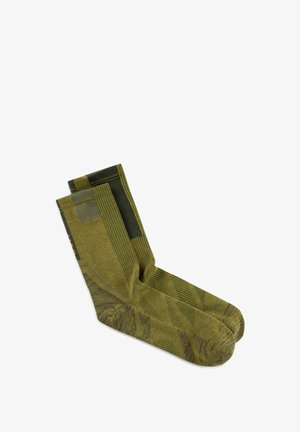 Paar grüne Socken bis zur Mitte der Wade mit geometrischen Mustern und gerippter Textur, flach auf weißem Hintergrund liegend.