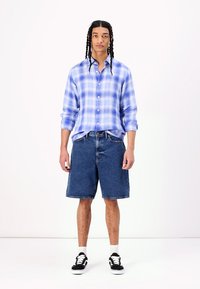 Light blue plaid shirt, denim shorts, black and white sneakers. The shirt has button closure and long sleeves; shorts are knee-length.