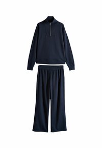 Tuta da uomo blu navy in tessuto morbido. Caratterizzato da un pullover con zip a un quarto e pantaloni larghi con elastico in vita.