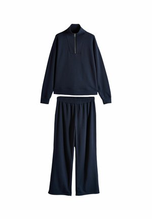 Tuta da uomo blu navy in tessuto morbido. Caratterizzato da un pullover con zip a un quarto e pantaloni larghi con elastico in vita.