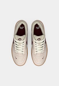 Tenisky Nike SB Force 58 majú svetlo béžový zvršok s tmavým marhuľovým akcentom a perforovanou špičkou; biele šnúrky a gumená podrážka.