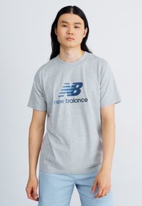 Gray short-sleeve T-shirt made of cotton, featuring a blue New Balance logo on the front. Simple, classic design with a relaxed fit.